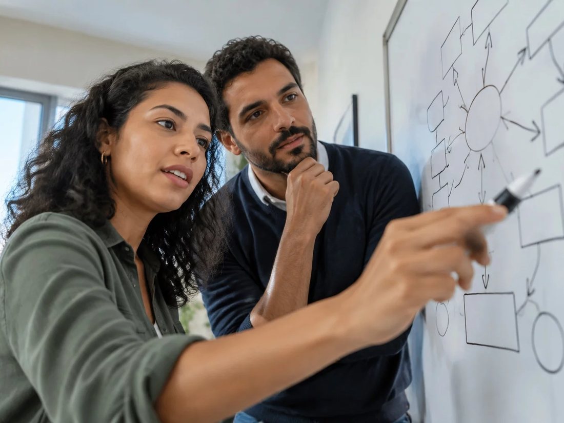 Dois alunos em pé diante do quadro branco, desenhando a ordem de um argumento